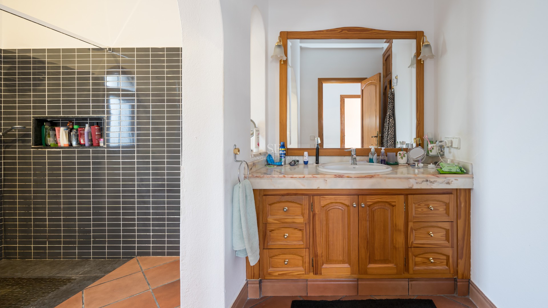 Bathroom featuring a wooden vanity with marble top, terracotta floor tiles, and a walk-in shower with dark grey tiles.