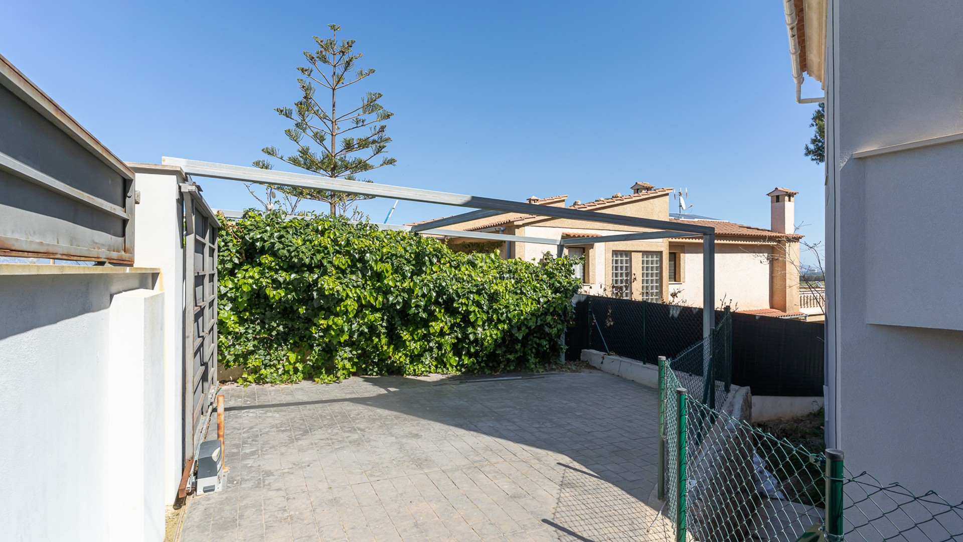 Stenlagd privat parkeringsplats med automatisk skjutgrind och en metallstomme för pergola.