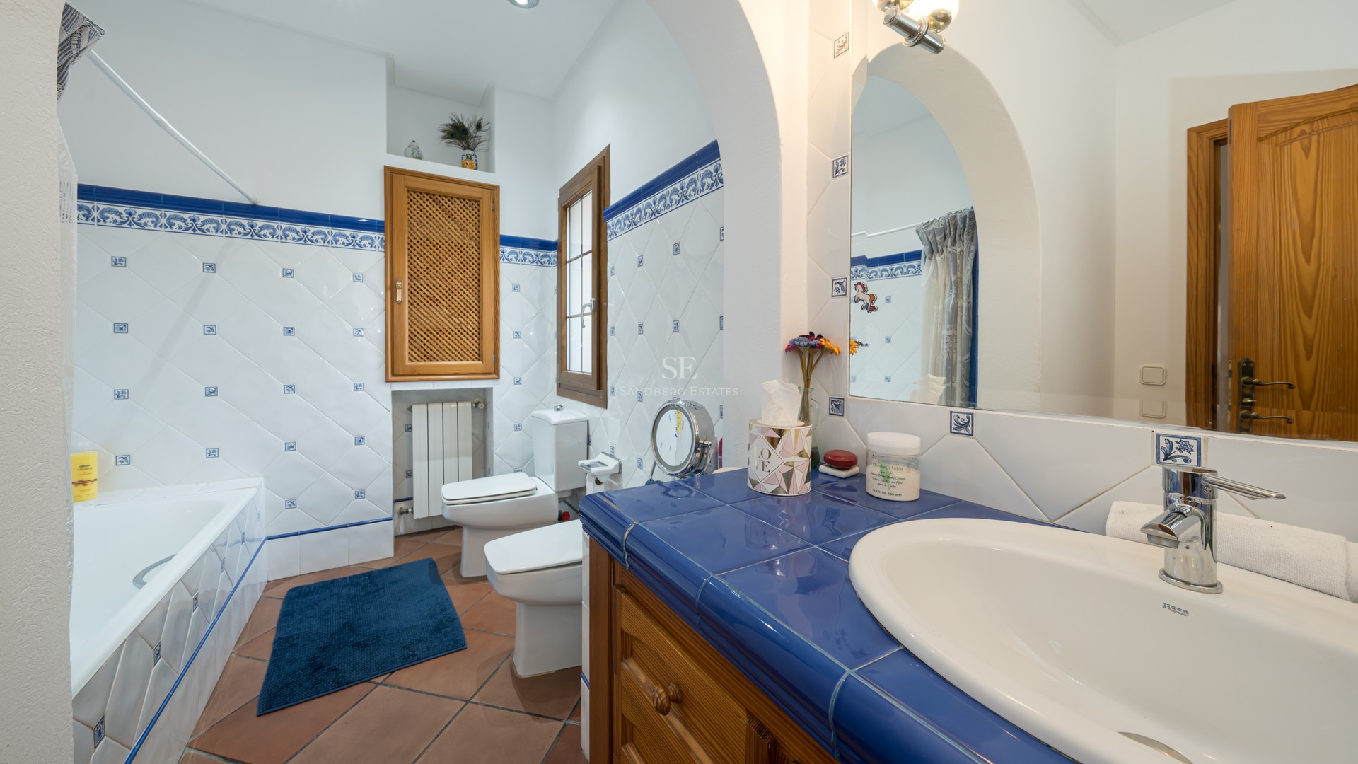 Bathroom featuring blue and white decorative tiling, terracotta floors, wooden vanity, and white ceramic fixtures.