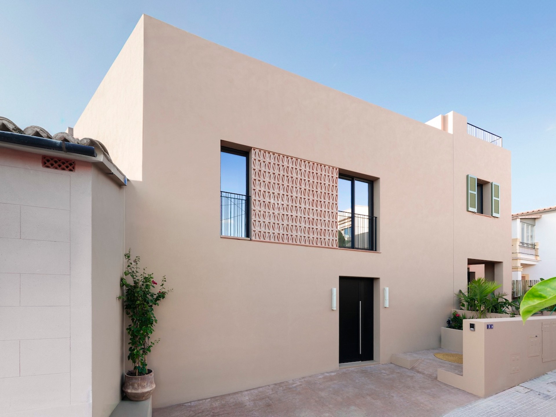 Façade beige avec porte noire, fenêtres à balustrades et écran décoratif en terre cuite.
