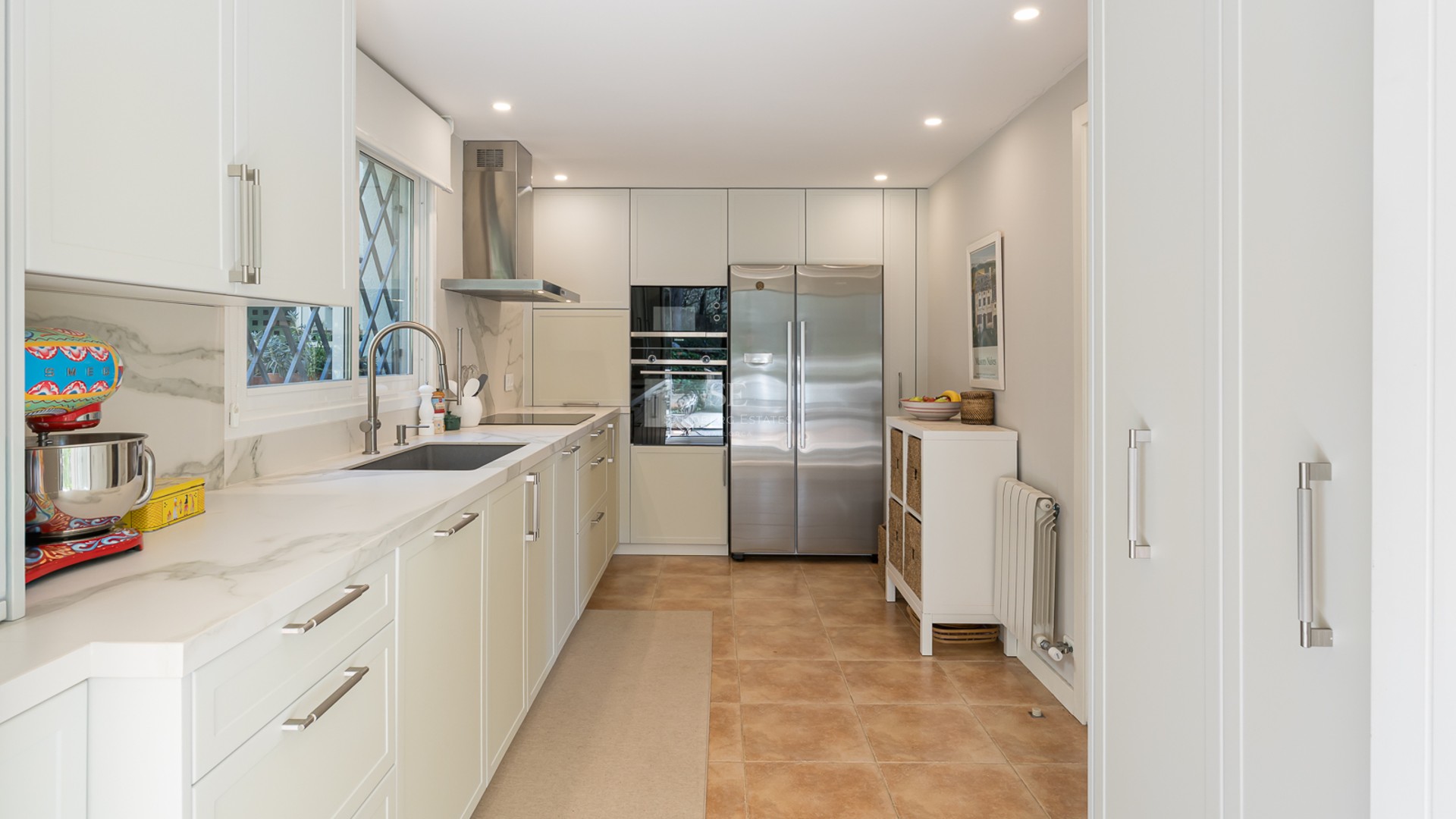 Contemporary galley kitchen featuring white cabinetry, marble countertops, stainless steel appliances, and terracotta floors.