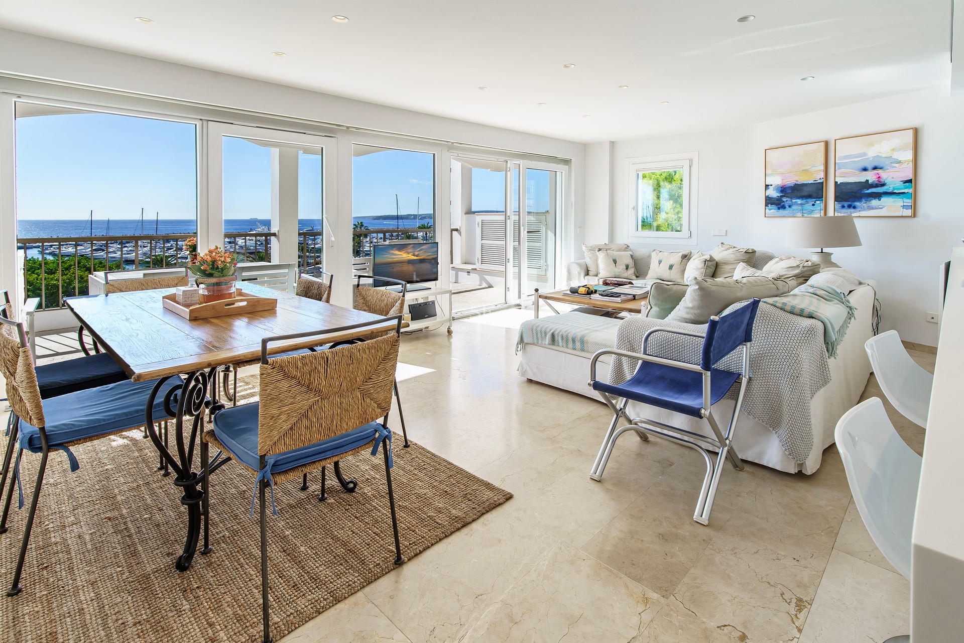 Open-plan living room with marble floors and large windows overlooking a marina and sea.