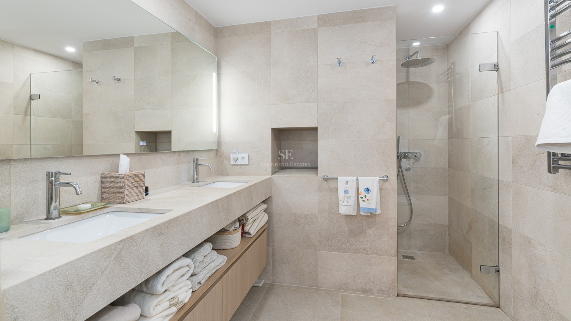 Modern bathroom featuring a double stone vanity, wood cabinets, and a walk-in glass shower with beige tiling.