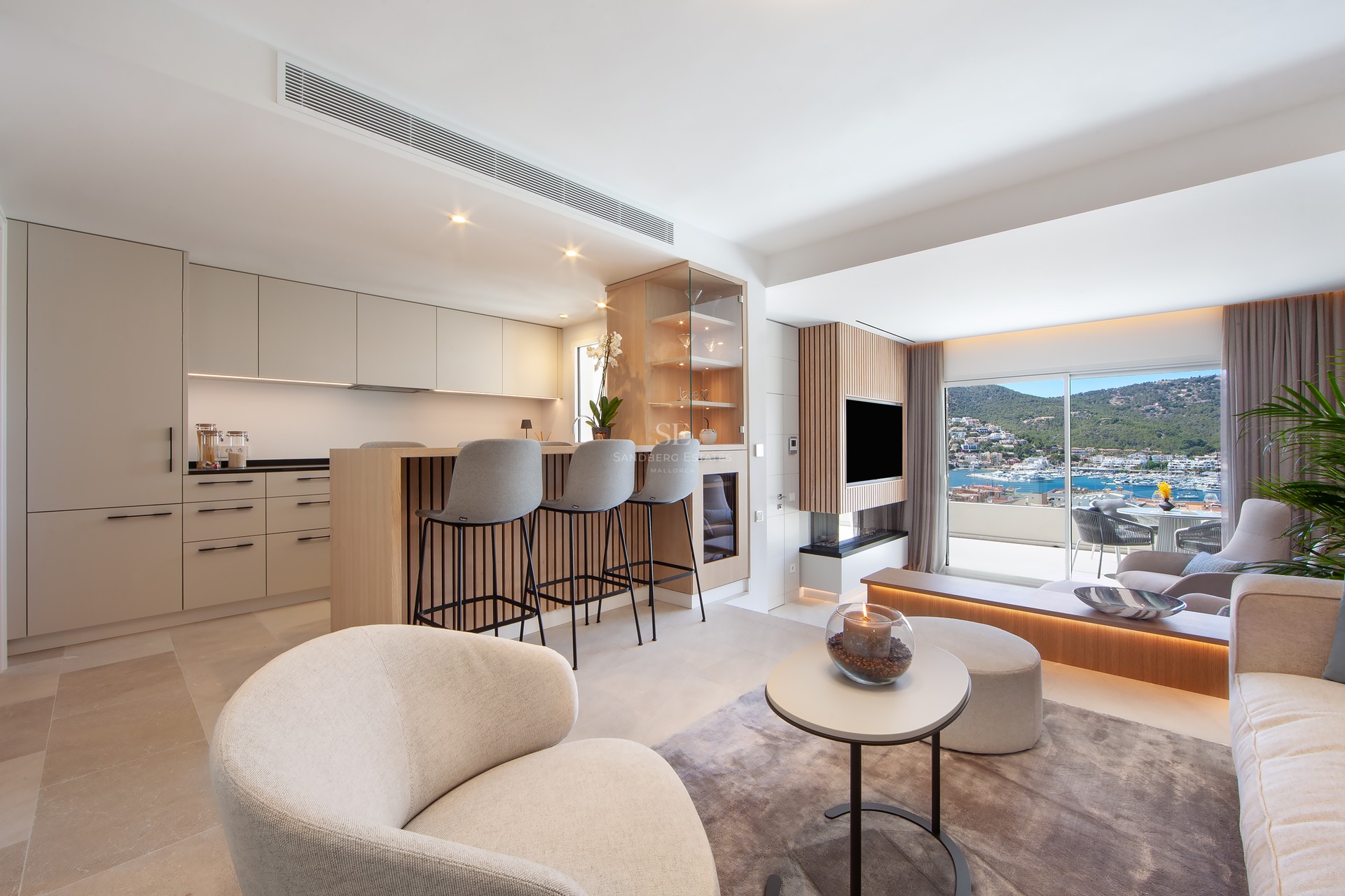 Salon et cuisine ouverts et modernes avec des armoires beiges et une grande fenêtre donnant sur un port de plaisance.