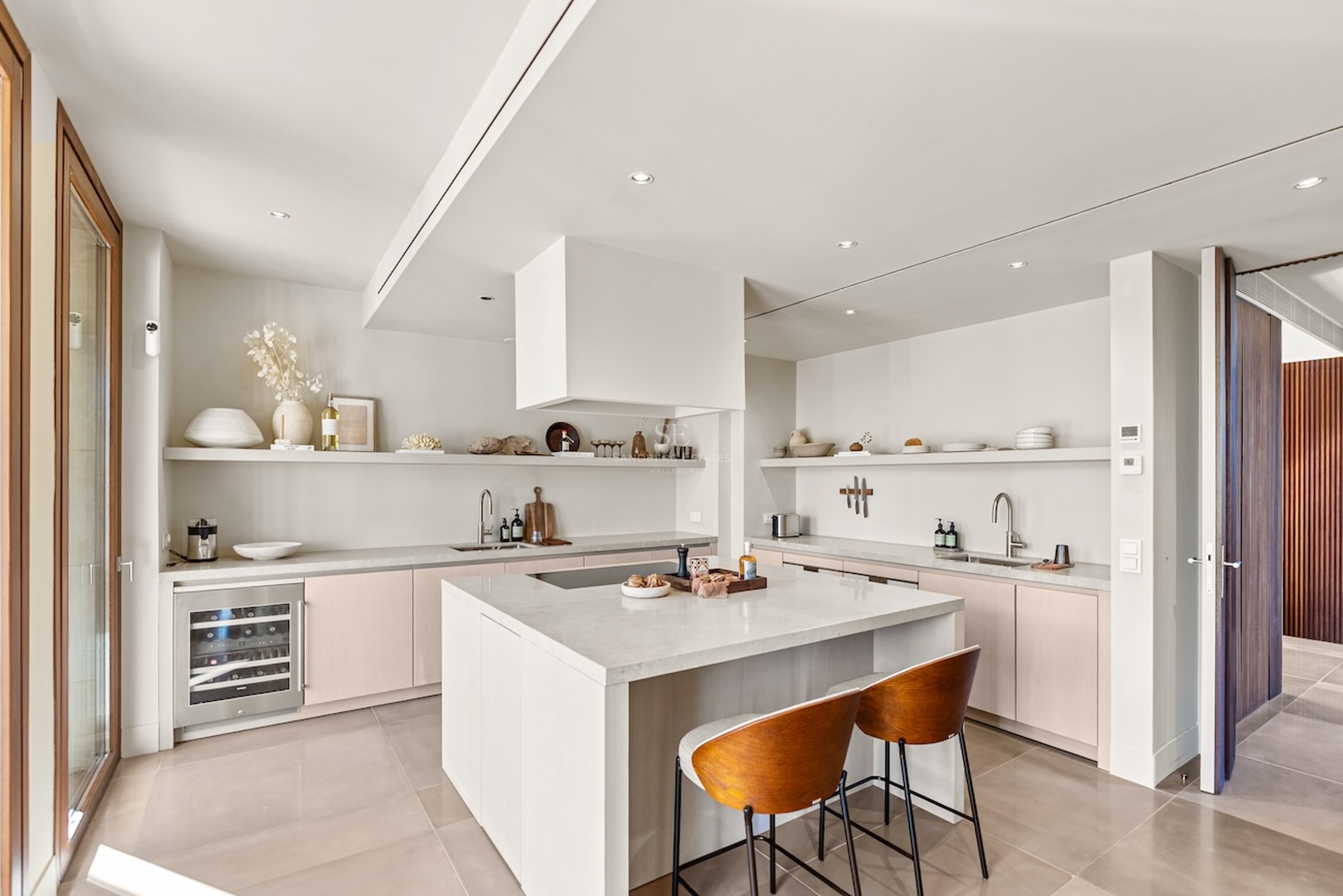 Cuisine moderne lumineuse avec îlot blanc, plans de travail en pierre, cave à vin et taburets en bois.