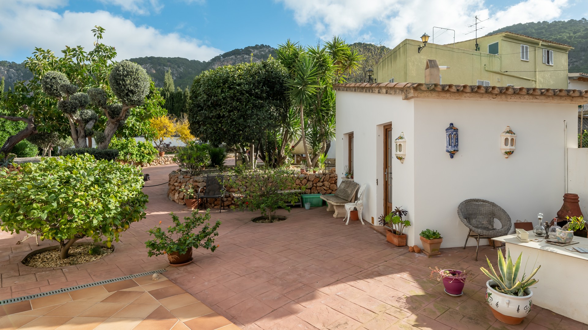 Sun-drenched terracotta patio featuring a whitewashed annex, lush Mediterranean gardens, and mountain views.