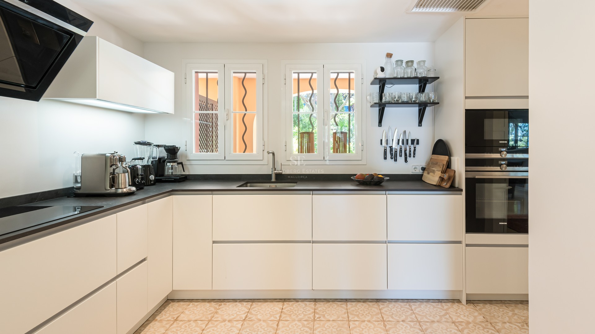Modern white kitchen featuring dark countertops, integrated Siemens appliances, and traditional patterned tile flooring.
