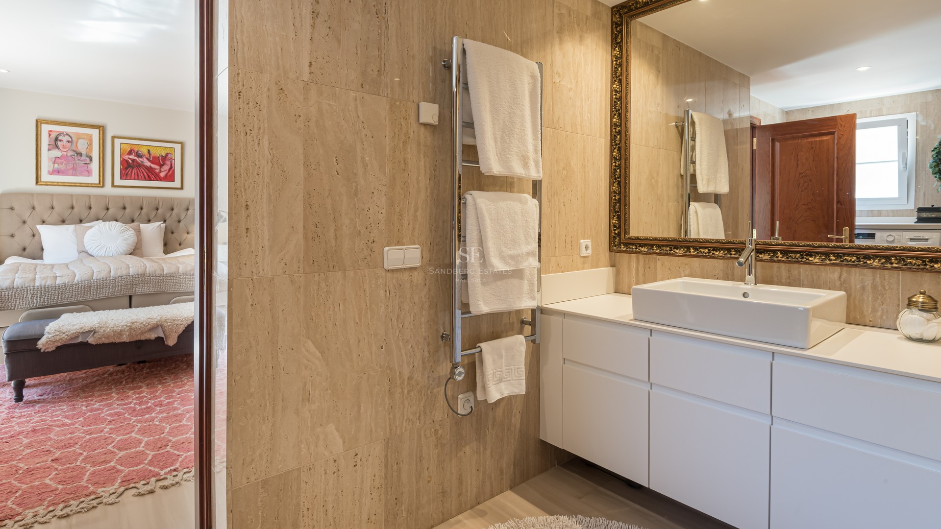 Modern bathroom with travertine stone walls, white vanity, vessel sink, and an ornate gold-framed mirror.