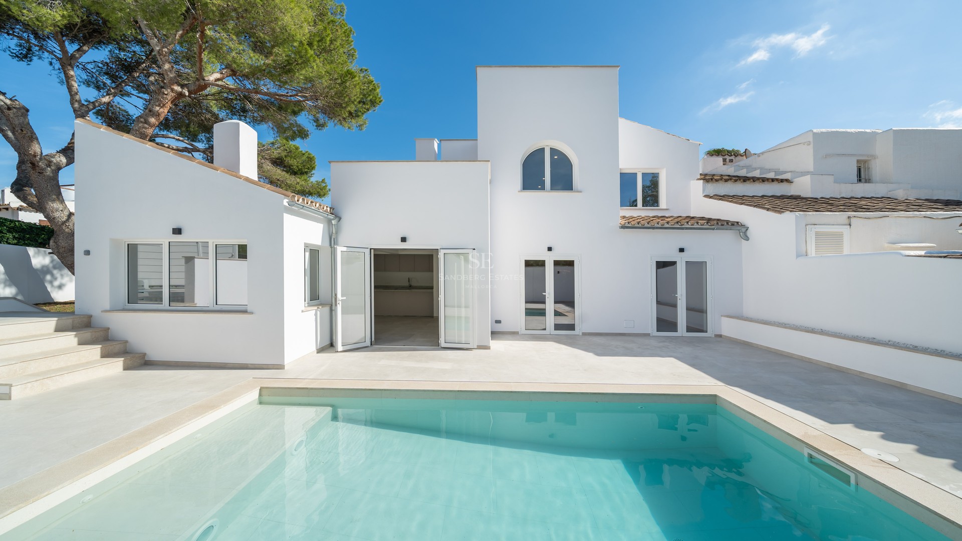 Piscine turquoise devant une villa blanche moderne au style méditerranéen sous un ciel pur.