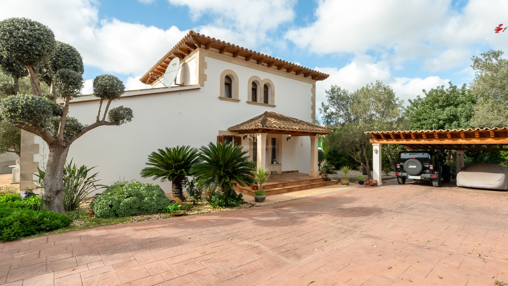 Two-story white Mediterranean villa with terracotta roof, arched windows, and a wide driveway with a carport.