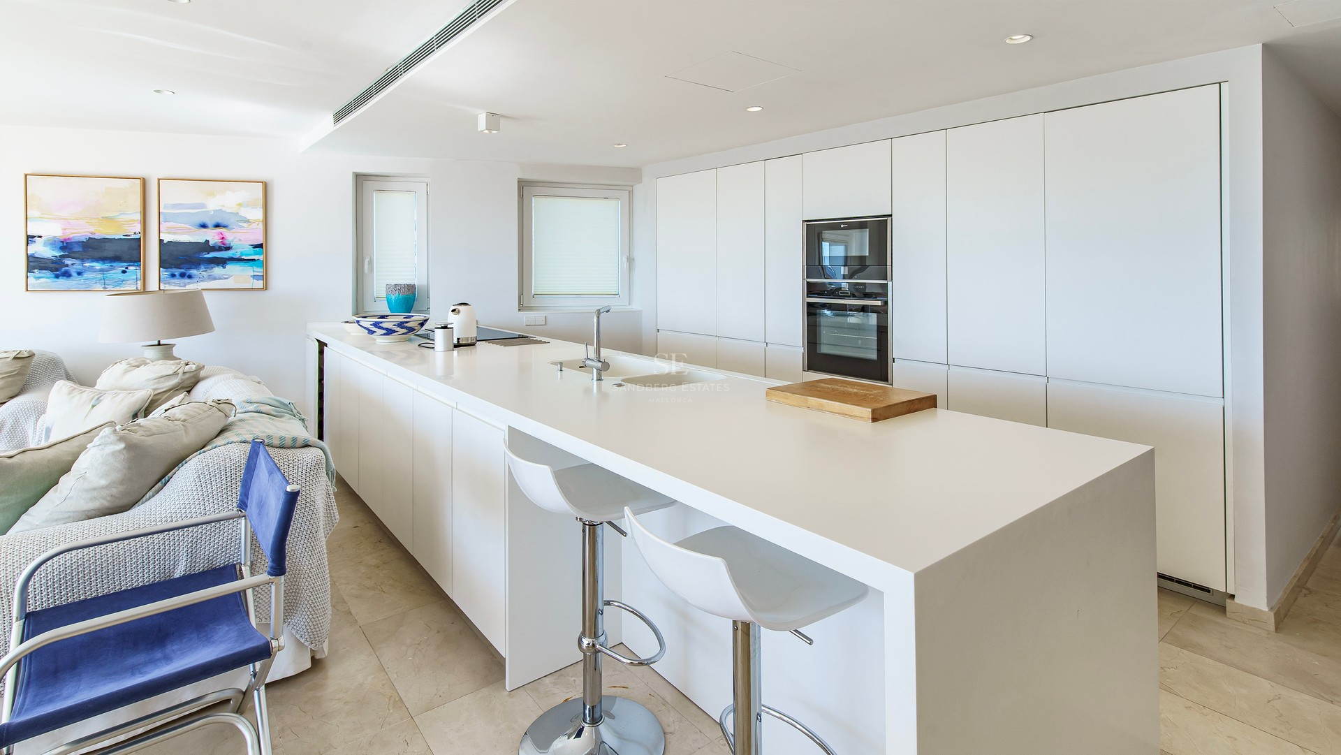 A bright, modern white kitchen featuring a large central island with bar stools and integrated appliances.