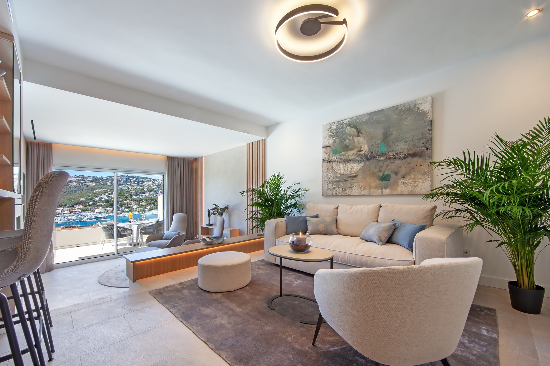 Salon moderne et lumineux avec mobilier crème, grandes baies vitrées sur la mer et plantes vertes.