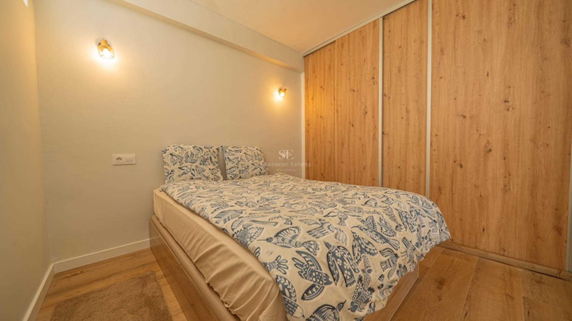 Dormitorio moderno con cama de textiles azules, armarios empotrados de madera de roble e iluminación de pared cálida.