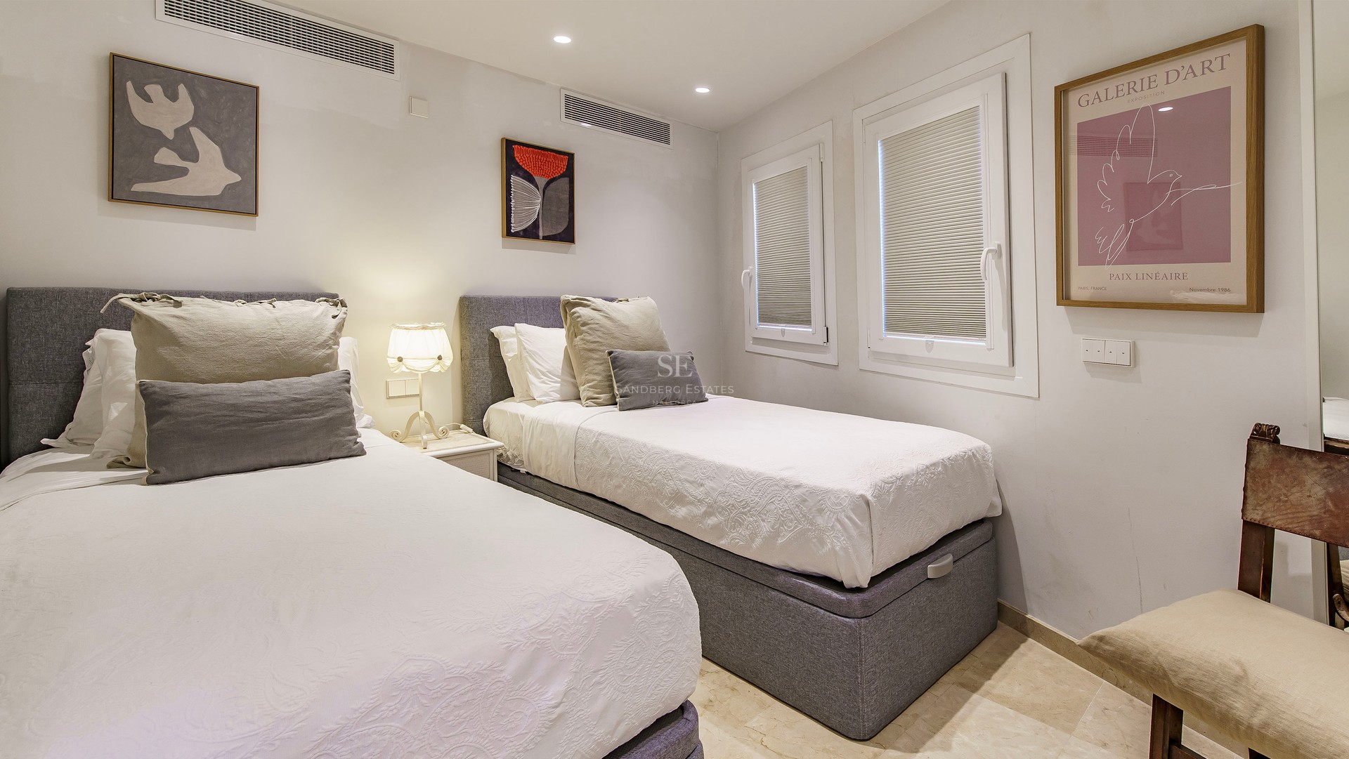 Bedroom with two single beds, grey headboards, white linens, and contemporary wall art.