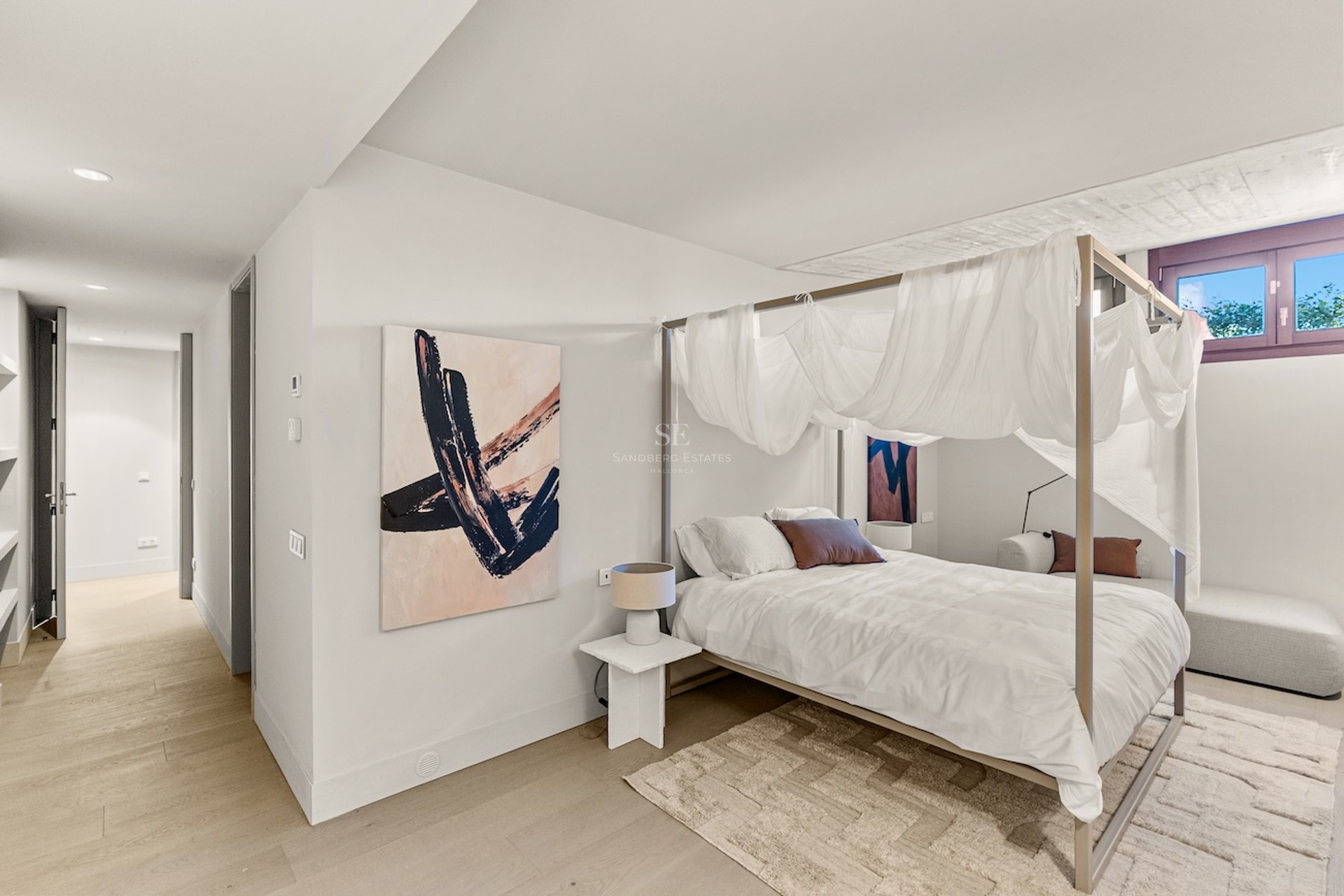 Chambre lumineuse dotée d'un lit à baldaquin avec voilages blancs, art abstrait et parquet clair.