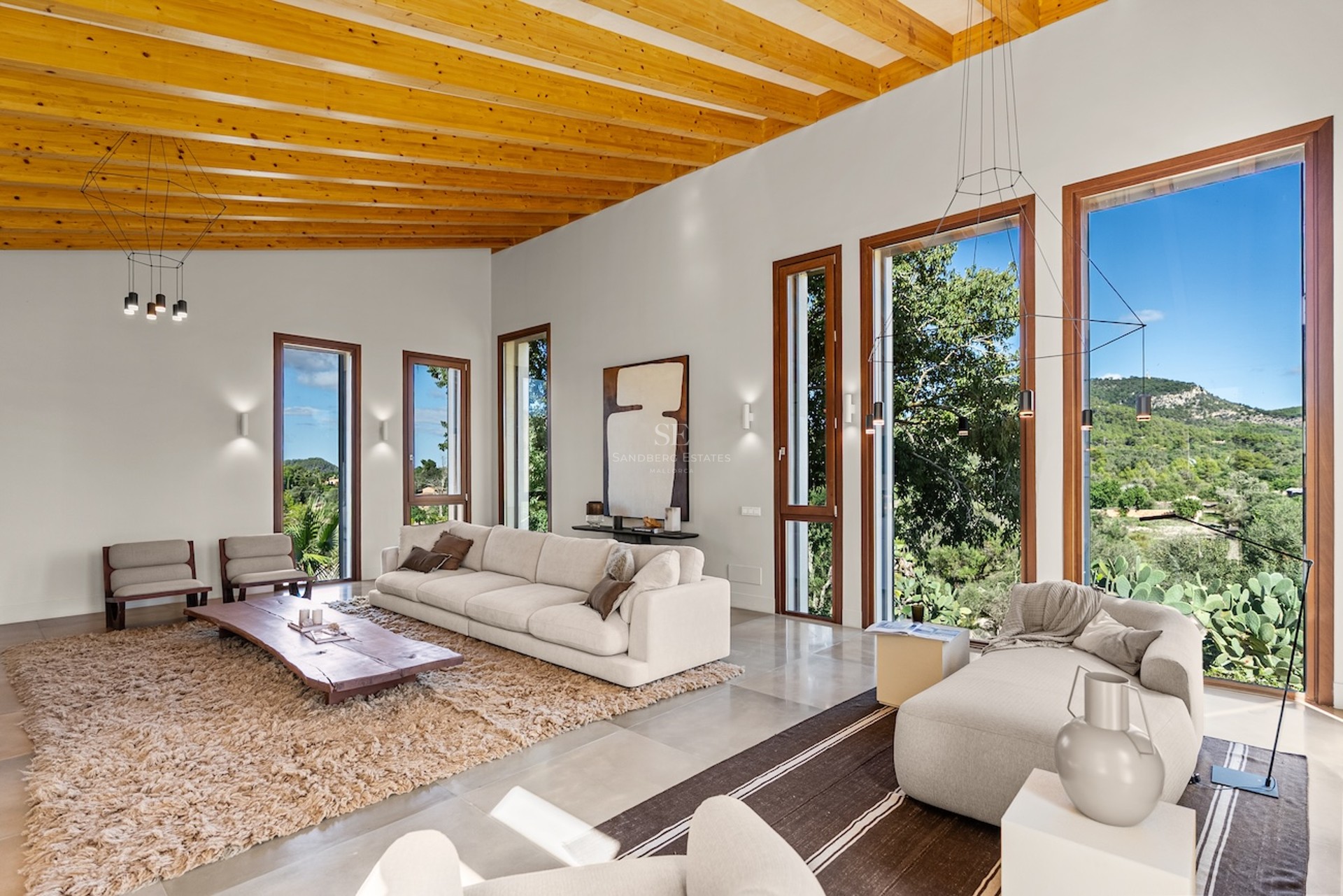 Grand salon moderne avec plafonds à poutres en bois, canapés blancs et grandes fenêtres donnant sur la montagne.