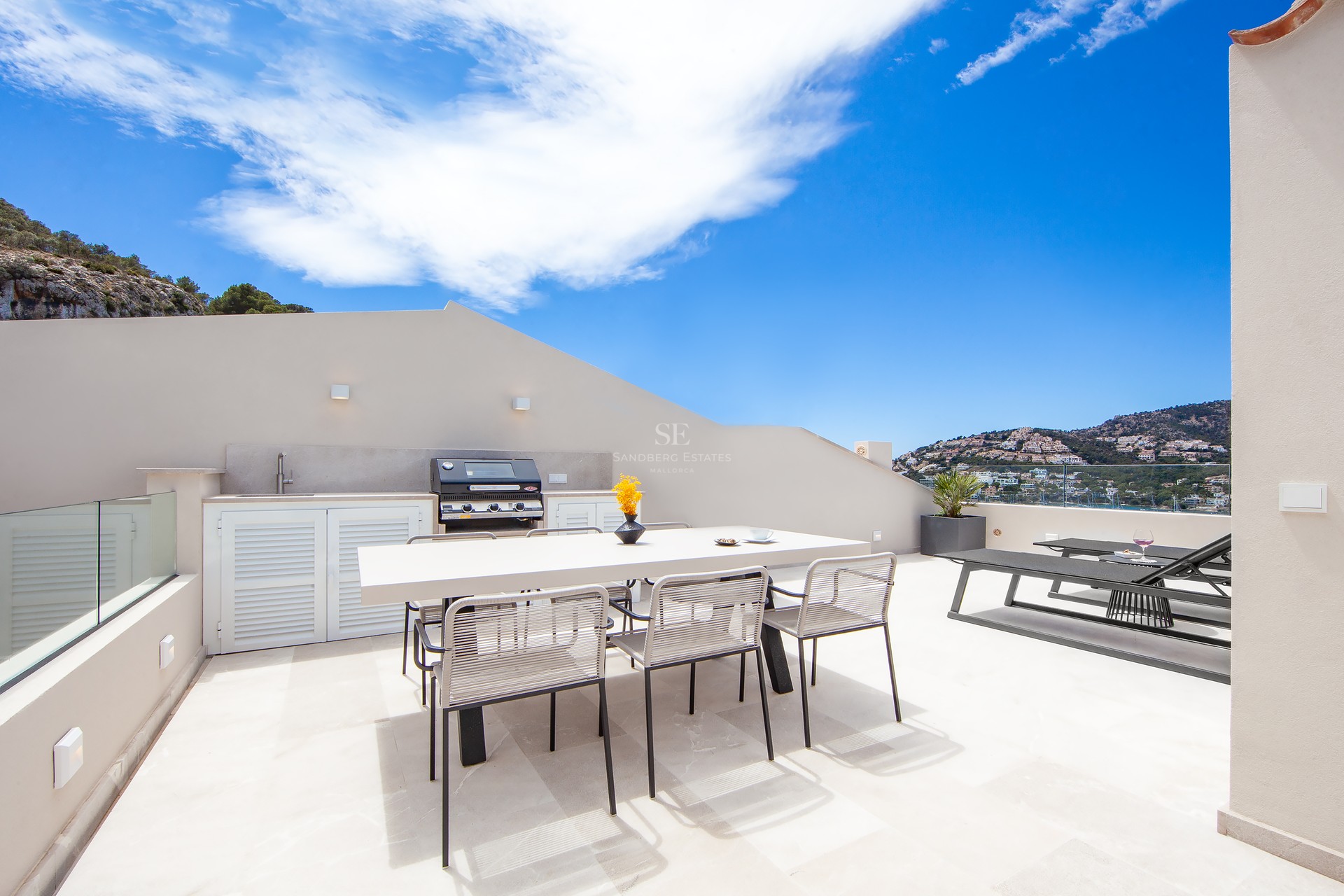 Terrasse moderne sur le toit avec cuisine extérieure, table à manger et transats avec vue panoramique.