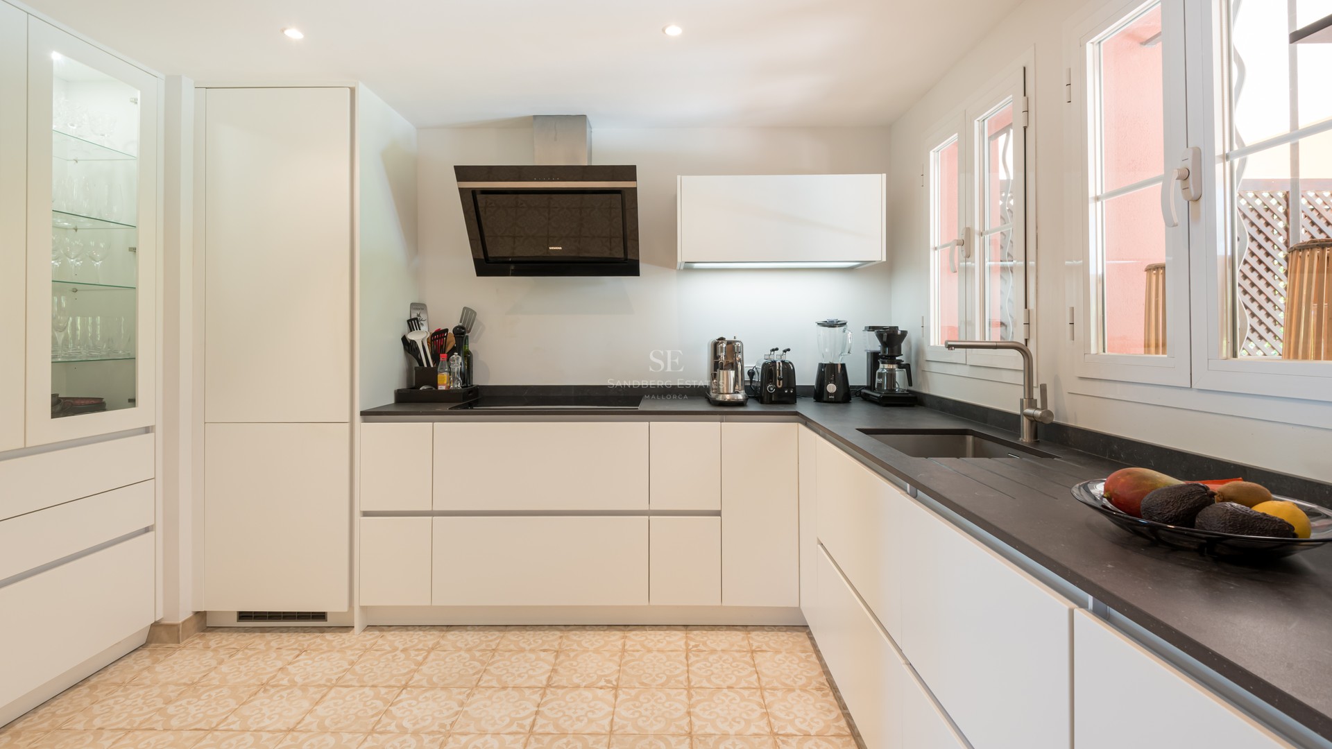 Contemporary kitchen featuring white handleless cabinets, dark stone countertops, and decorative patterned floor tiles.