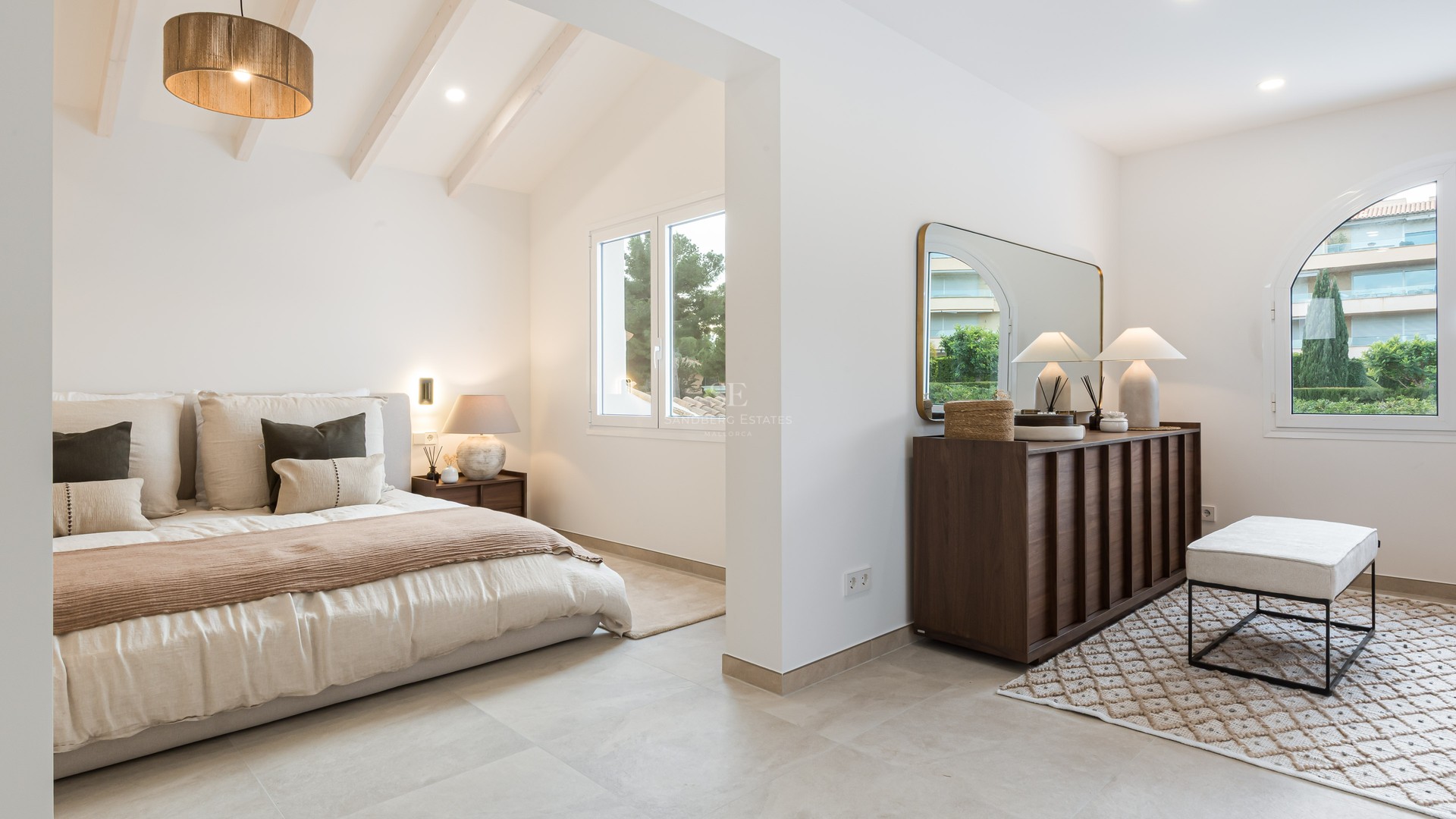 Chambre parentale moderne avec plafonds à poutres blanches, lit king-size, commode en bois sombre et lumière naturelle.