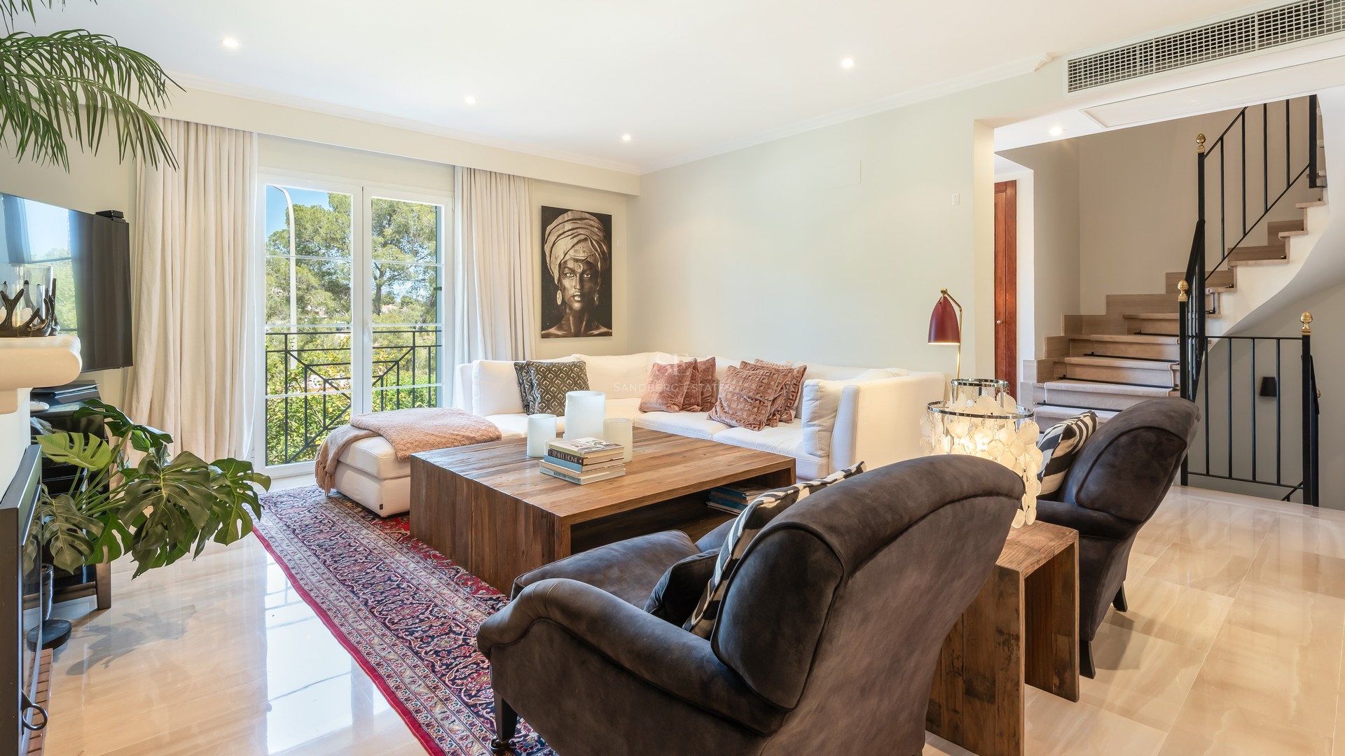 Sophisticated living room featuring a white sectional sofa, rustic wood table, marble floors, and garden views.