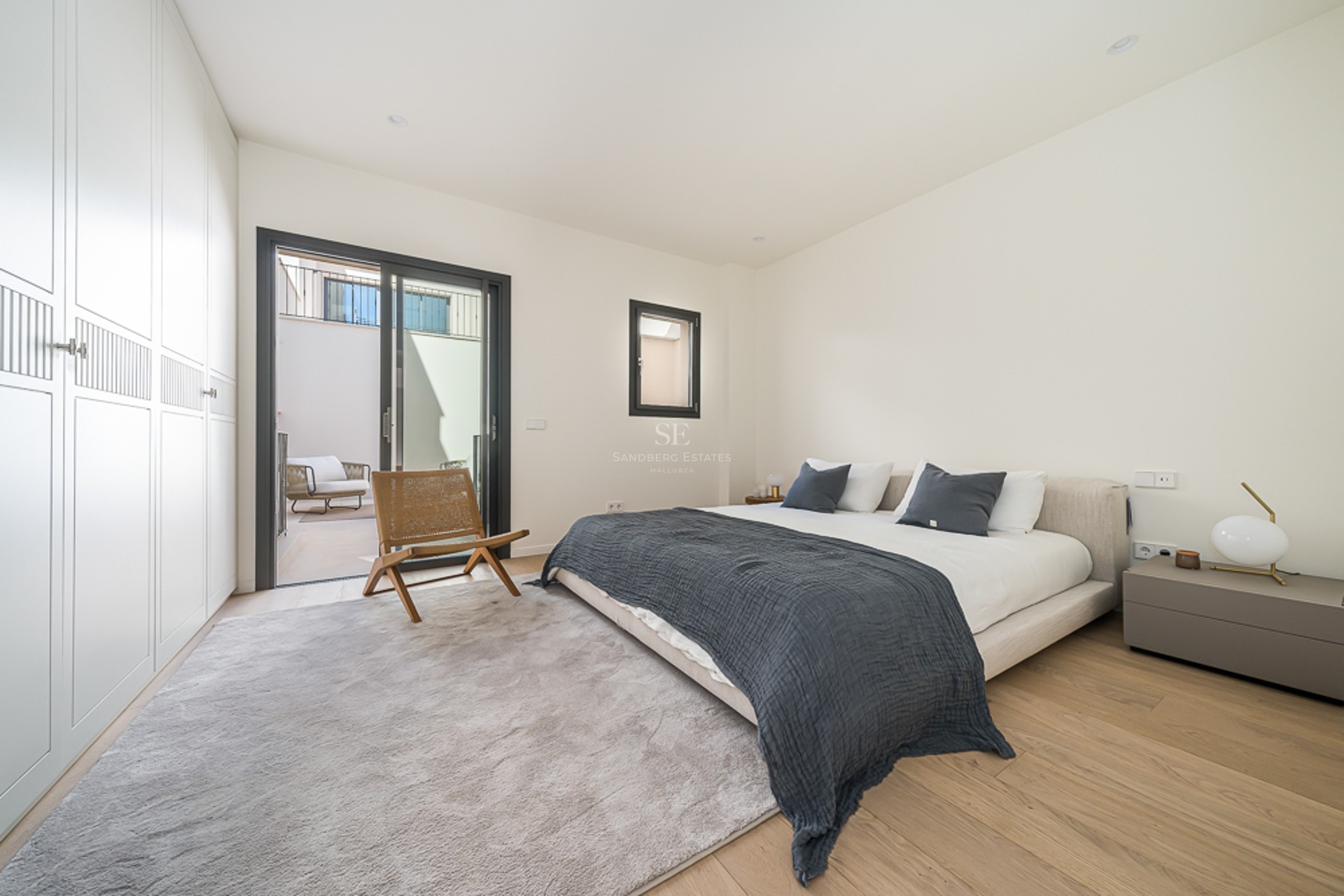 Bright master bedroom featuring floor-to-ceiling wardrobes, light oak floors, and sliding glass doors to a private patio.