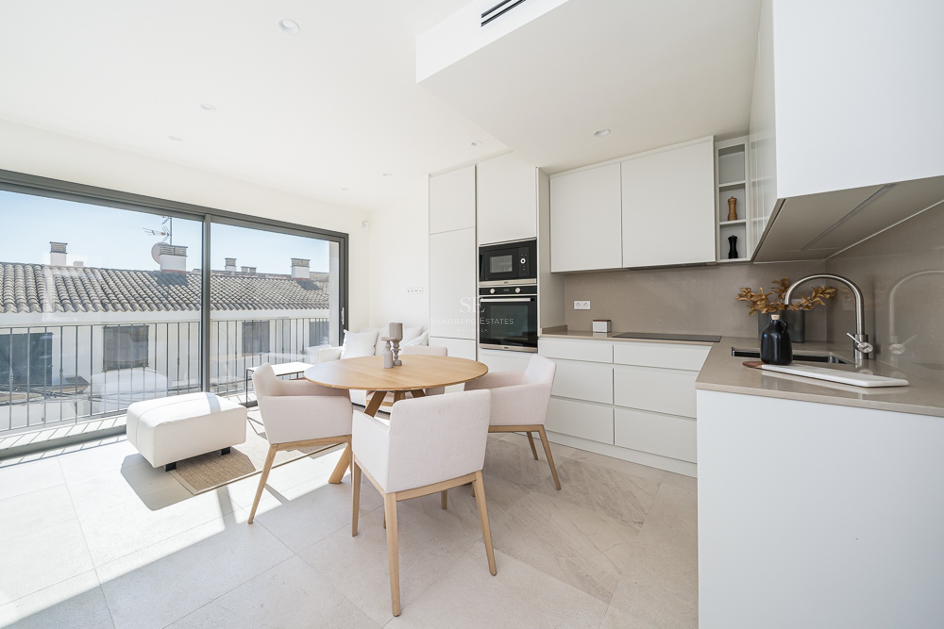 Bright kitchen with white cabinetry, wood dining table, and large glass doors overlooking traditional rooftops.
