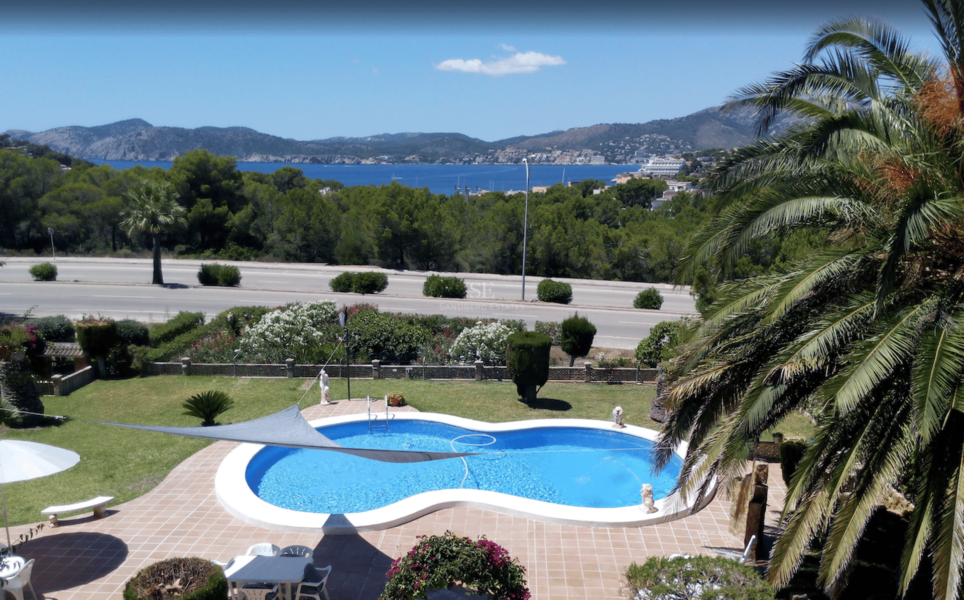Piscina en forma de riñón rodeada de terracota y jardín con vistas al Mediterráneo y las montañas.