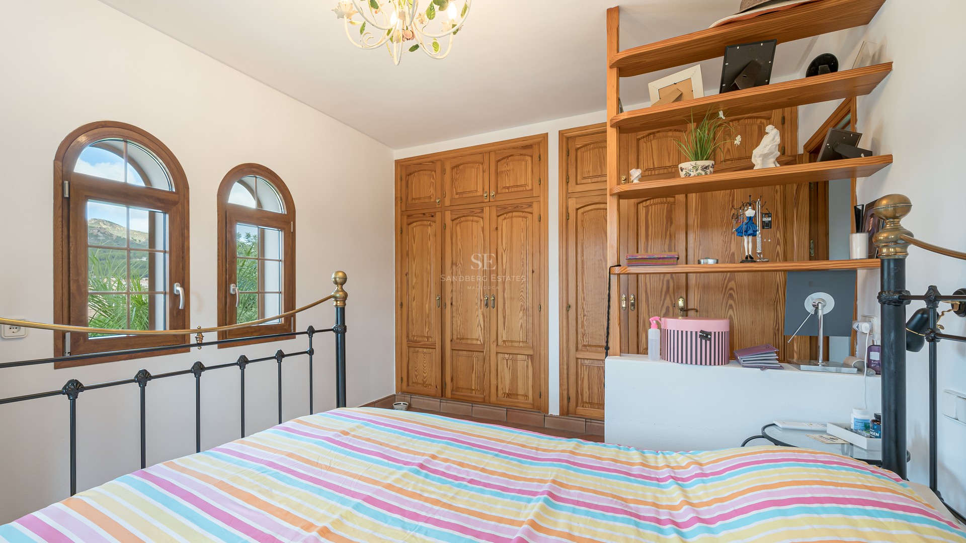 Bedroom featuring a wrought iron bed, large pine wardrobes, and arched windows with mountain views.