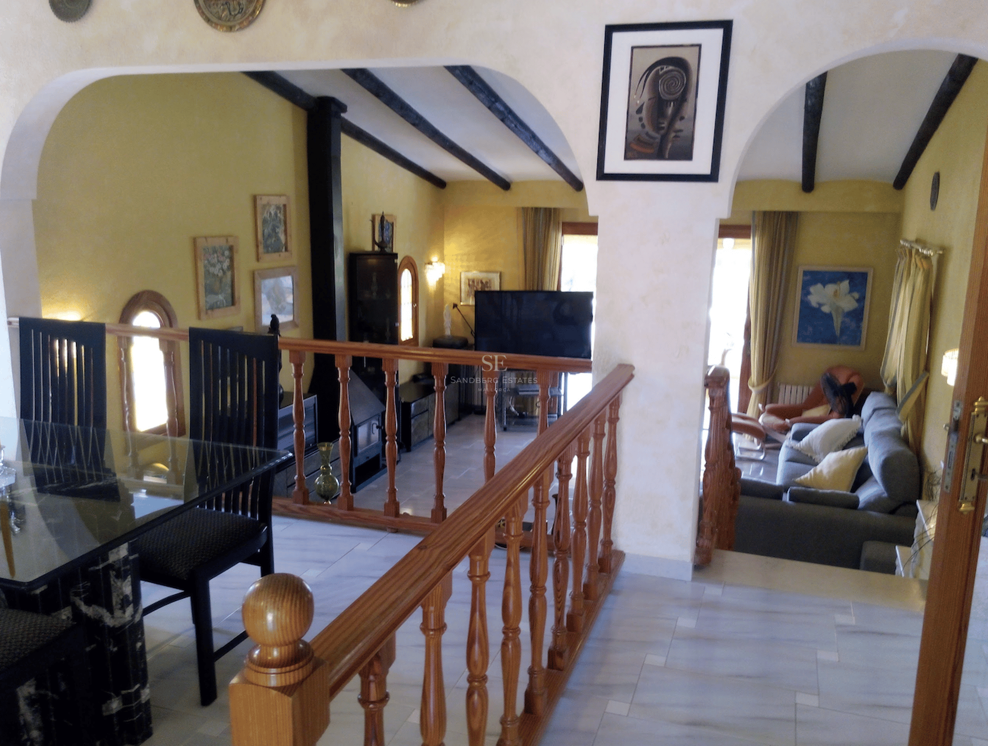 Interiör i två nivåer som visar en matplats med utsikt över ett nedsänkt vardagsrum med gula väggar och takbjälkar.