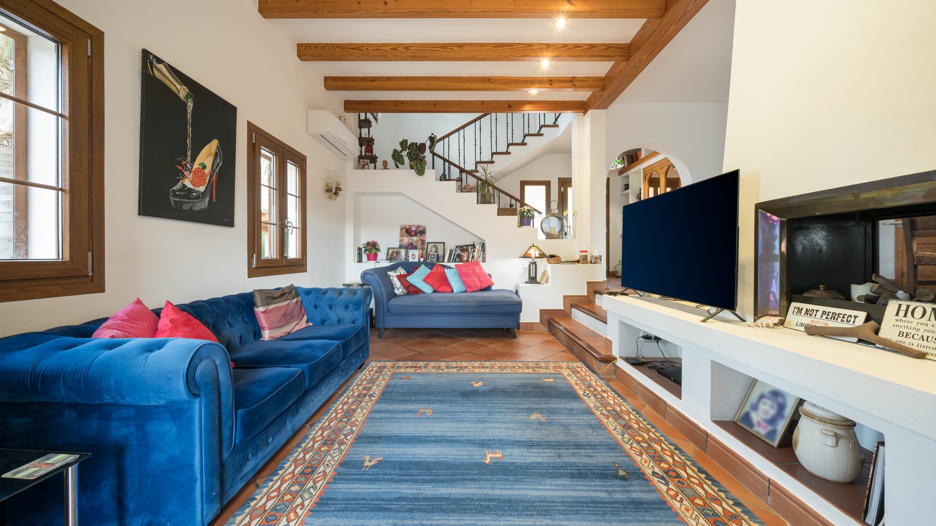 Spacious living room featuring blue velvet sofas, exposed wooden ceiling beams, and traditional terracotta floor tiles.