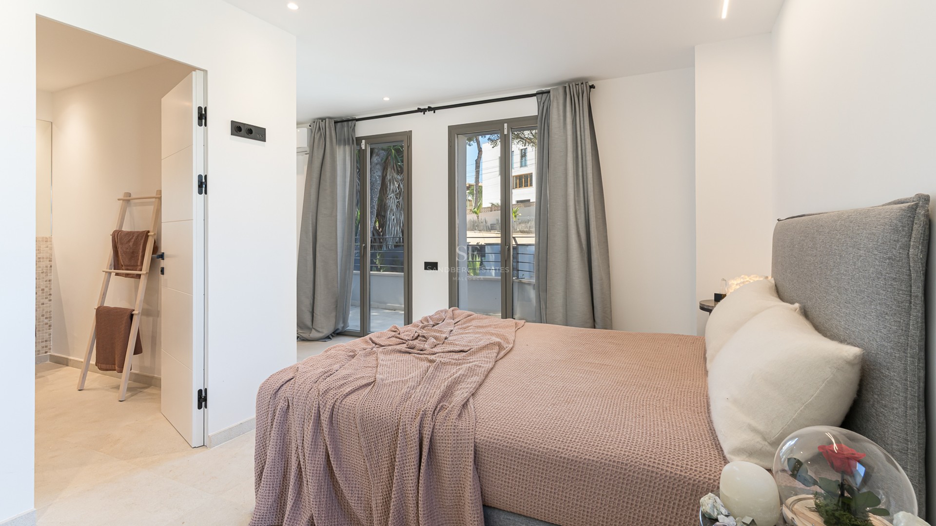 Modernt sovrum med grå stoppad säng, lila pläd, fönster från golv till tak och ingång till eget badrum.