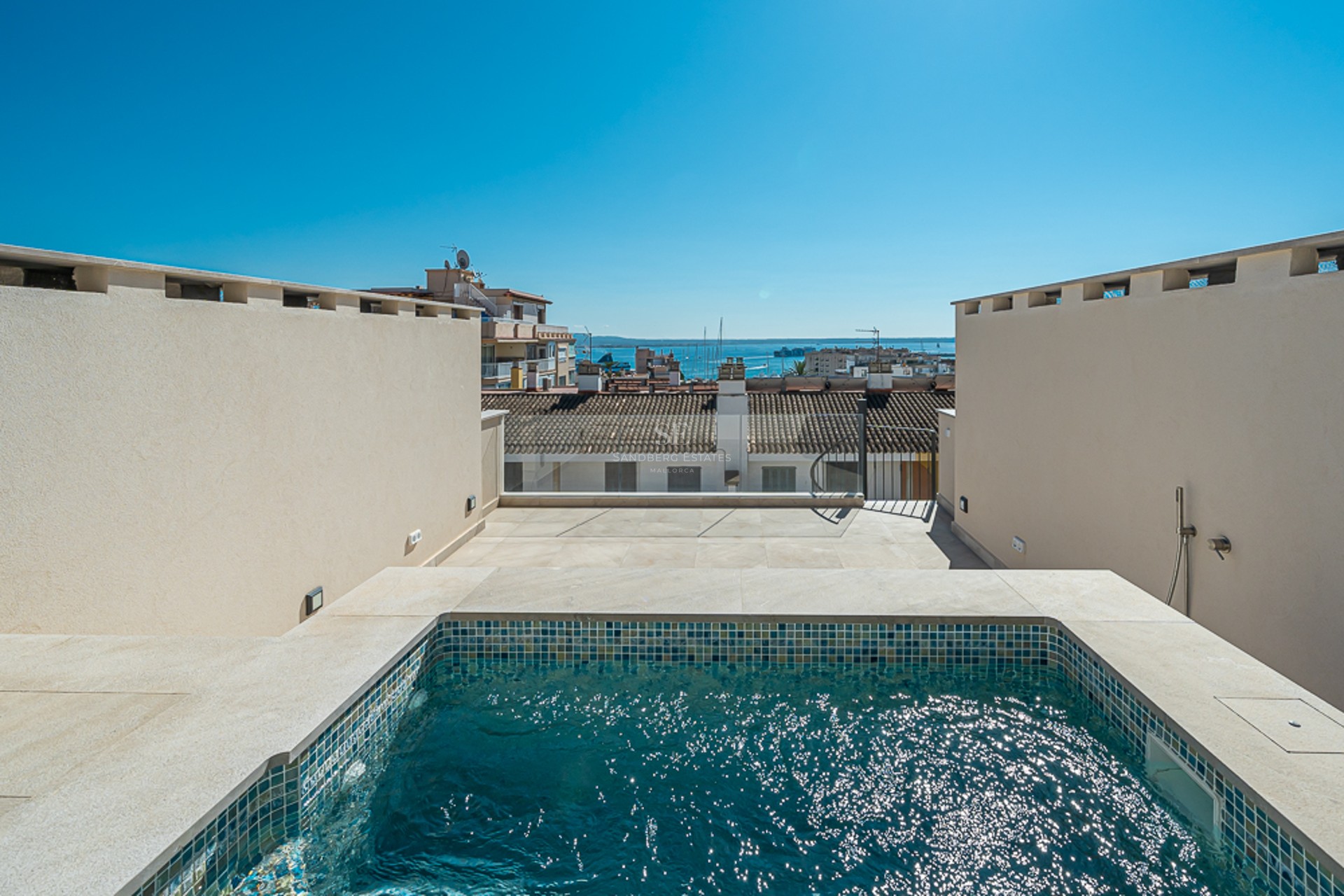 A private rooftop plunge pool featuring turquoise mosaic tiles and natural stone coping with views of a Mediterranean harbor.