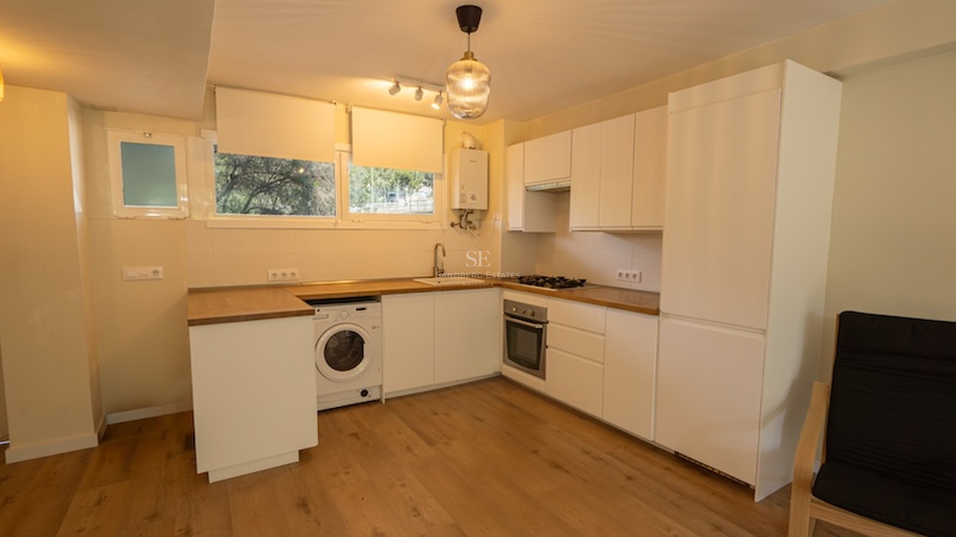 Cocina moderna blanca con encimeras de madera, lavadora integrada, horno y suelos laminados de madera.