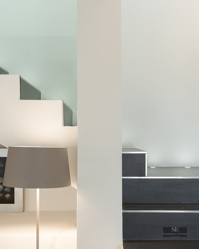 Close-up of a minimalist staircase with dark steps, white walls, and circular recessed floor lights.