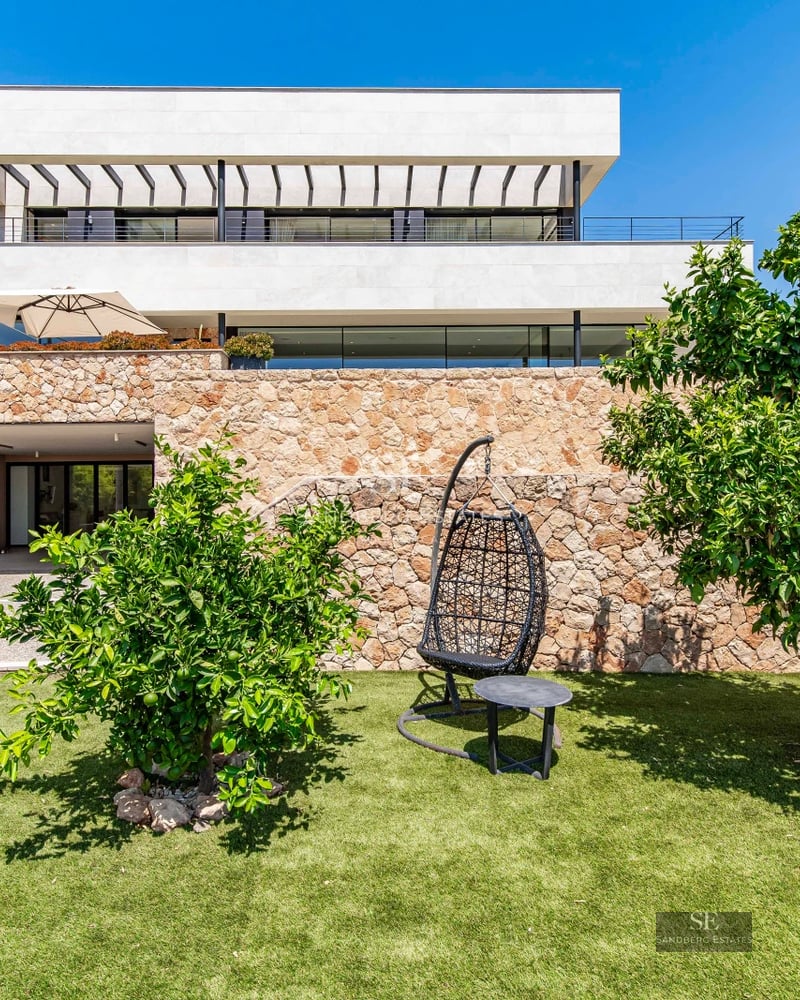 Exterior view of a modern house with a pool, sun loungers, and lush garden. Minimalist architecture with large windows.