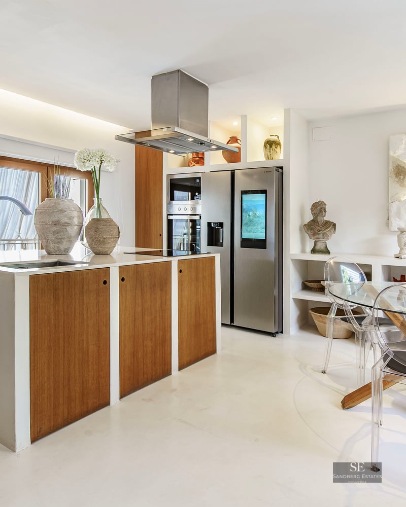 Modern kitchen featuring a wooden island, stainless steel appliances, and a glass dining table with clear acrylic chairs.
