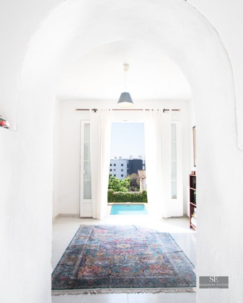 A view through a white plastered archway into a bright room with a colorful oriental rug and a pool visible outside.