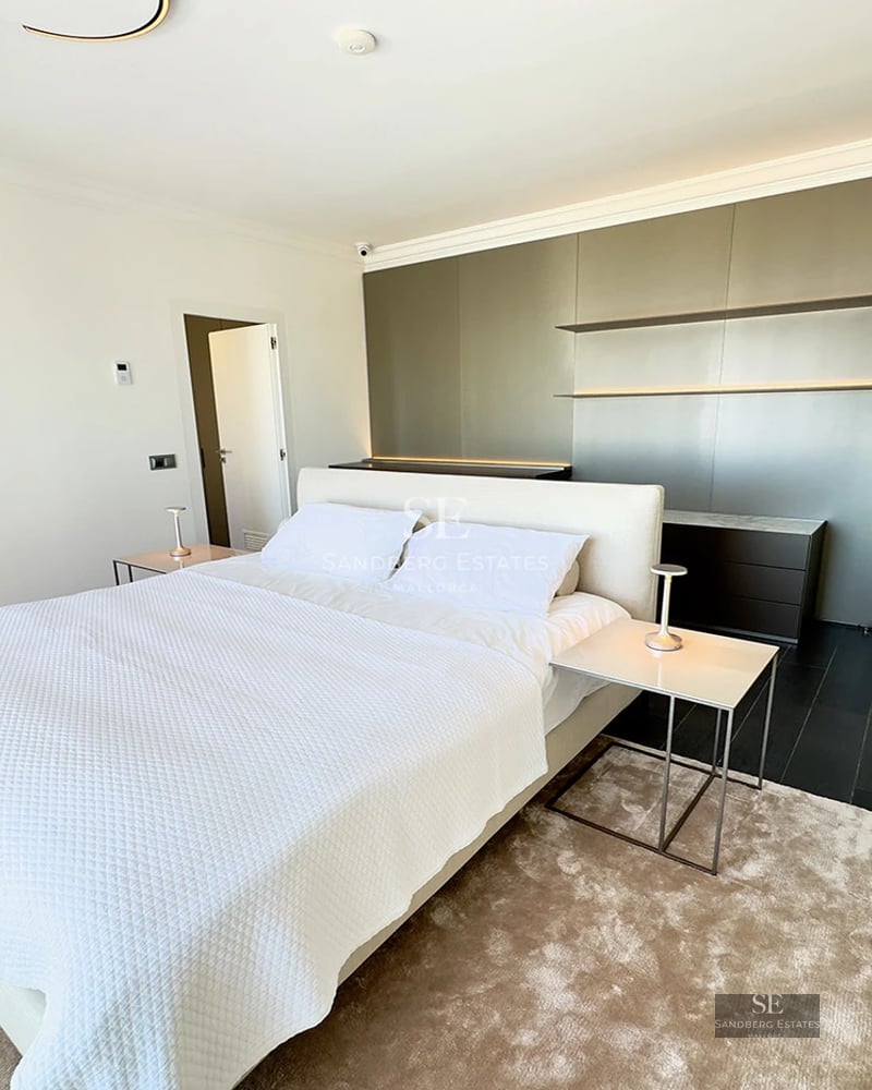 Sleek modern master bedroom featuring a large white bed, plush rug, and a minimalist grey feature wall with lighting.
