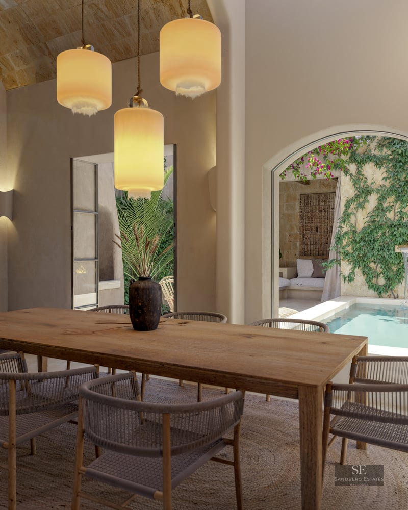 A large wooden dining table with woven chairs under three pendant lights, looking out to a courtyard plunge pool.