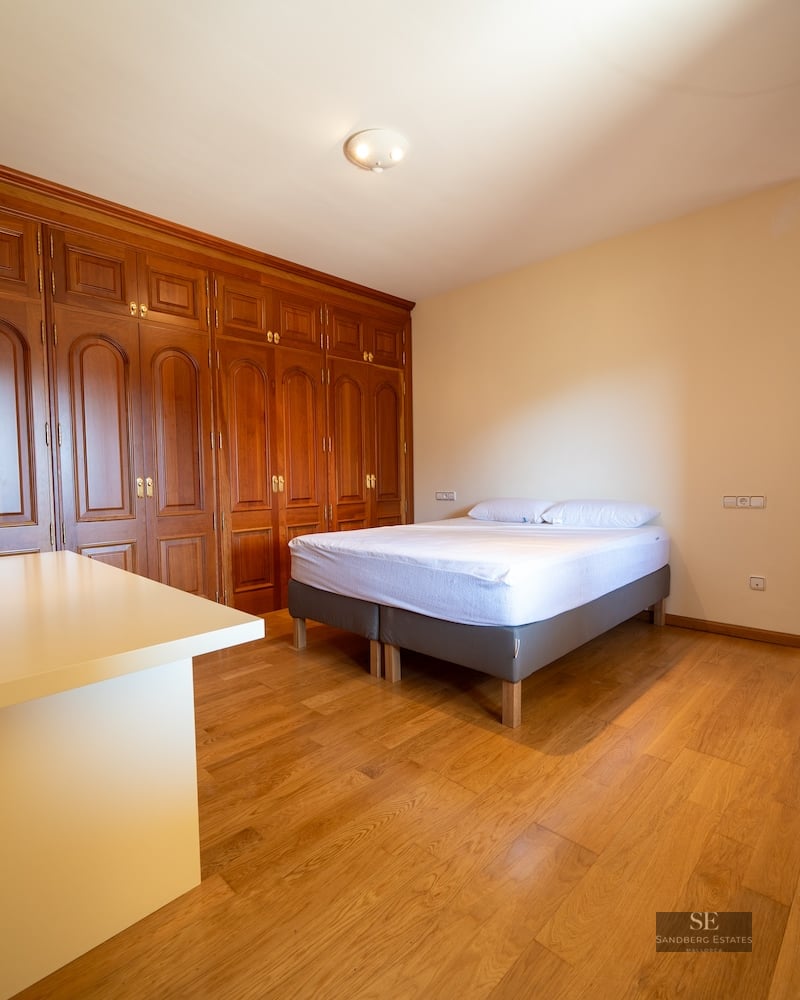 Bright bedroom featuring large built-in wooden closets, hardwood floors, and a minimalist double bed.