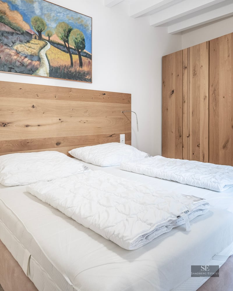 Modern bedroom with a large oak wardrobe, wooden headboard, and a double bed with crisp white linens.