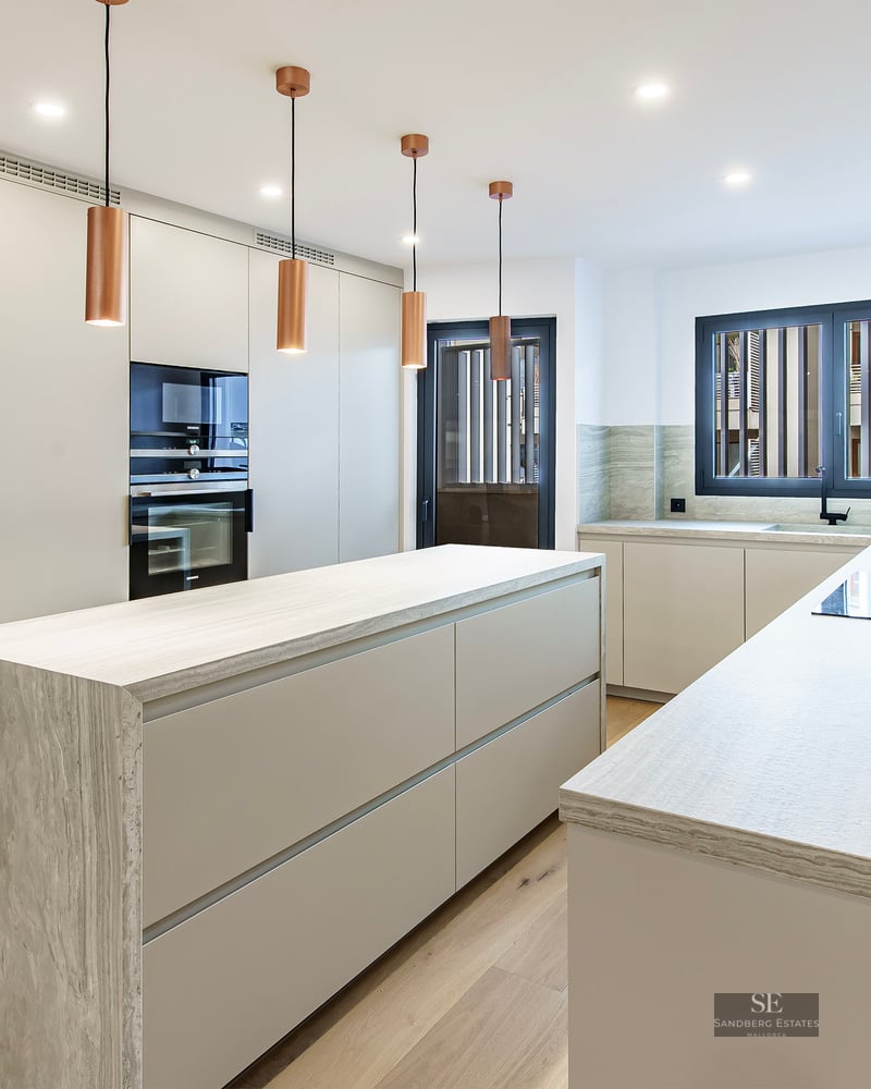 Cuisine contemporaine blanche avec îlot en pierre, suspensions en cuivre et parquet en bois.