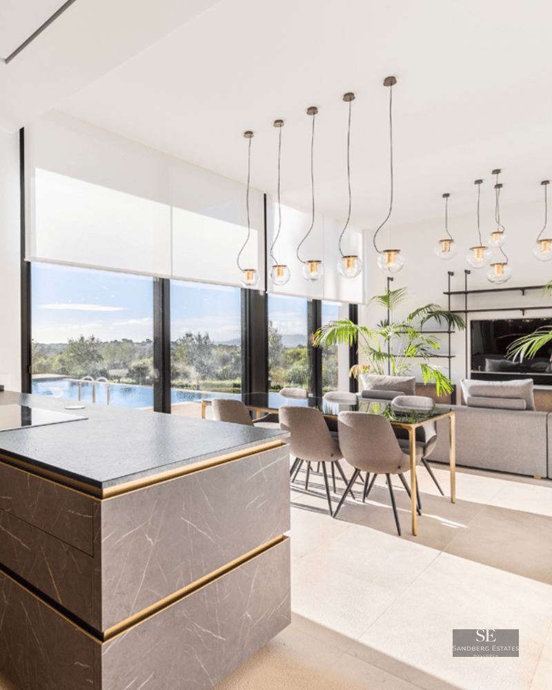 Spacious open-concept living room with a stone kitchen island, dining table, and large windows overlooking a pool.