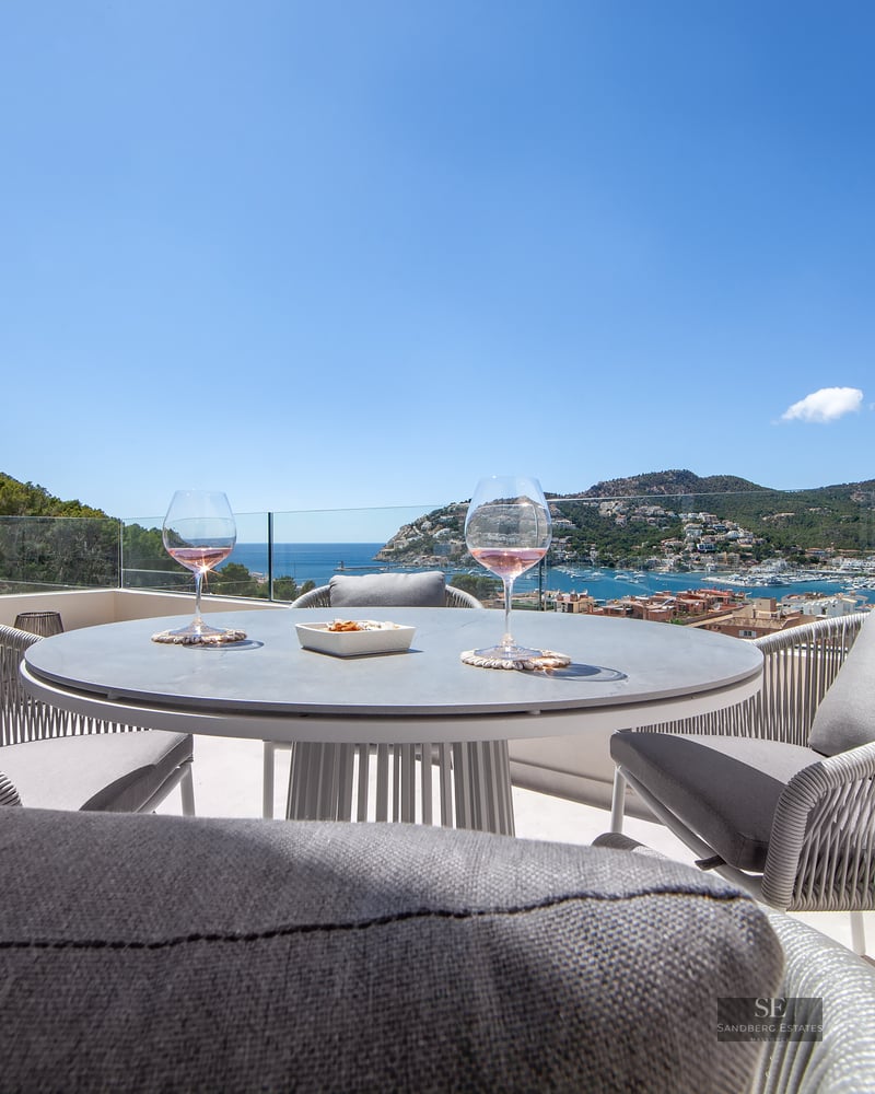 Modern terrace table with two glasses of wine set against a spectacular view of the harbor and sea under a clear blue sky.
