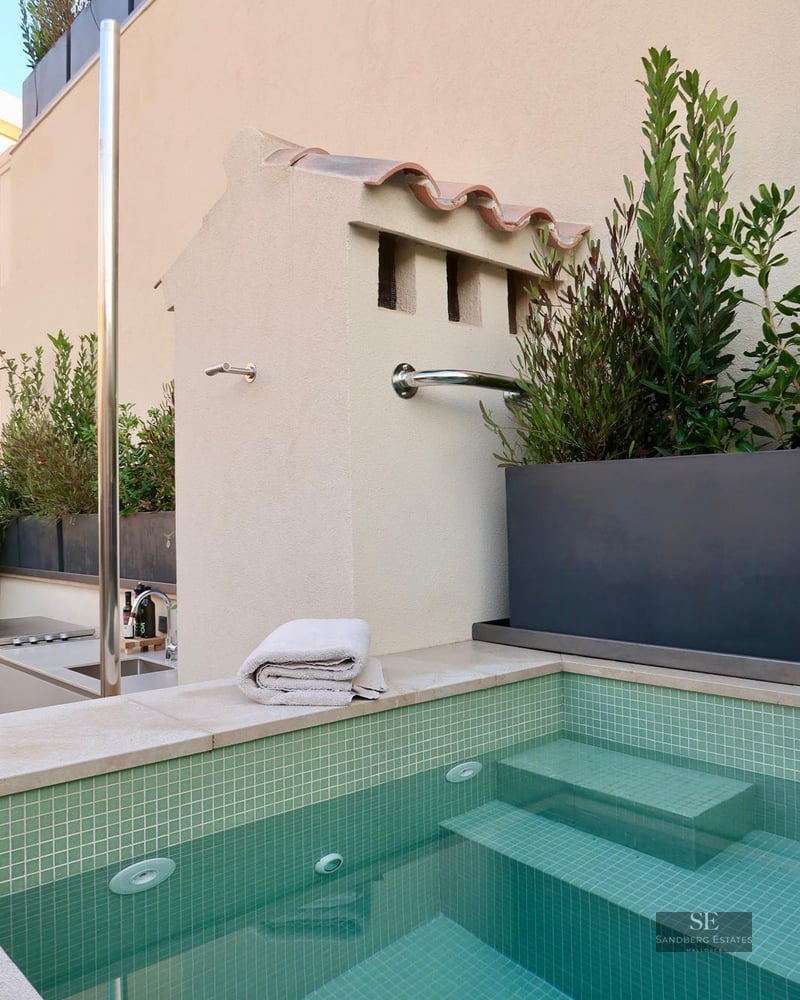 Green mosaic tile pool with submerged steps and a stainless steel shower next to a light-colored wall.