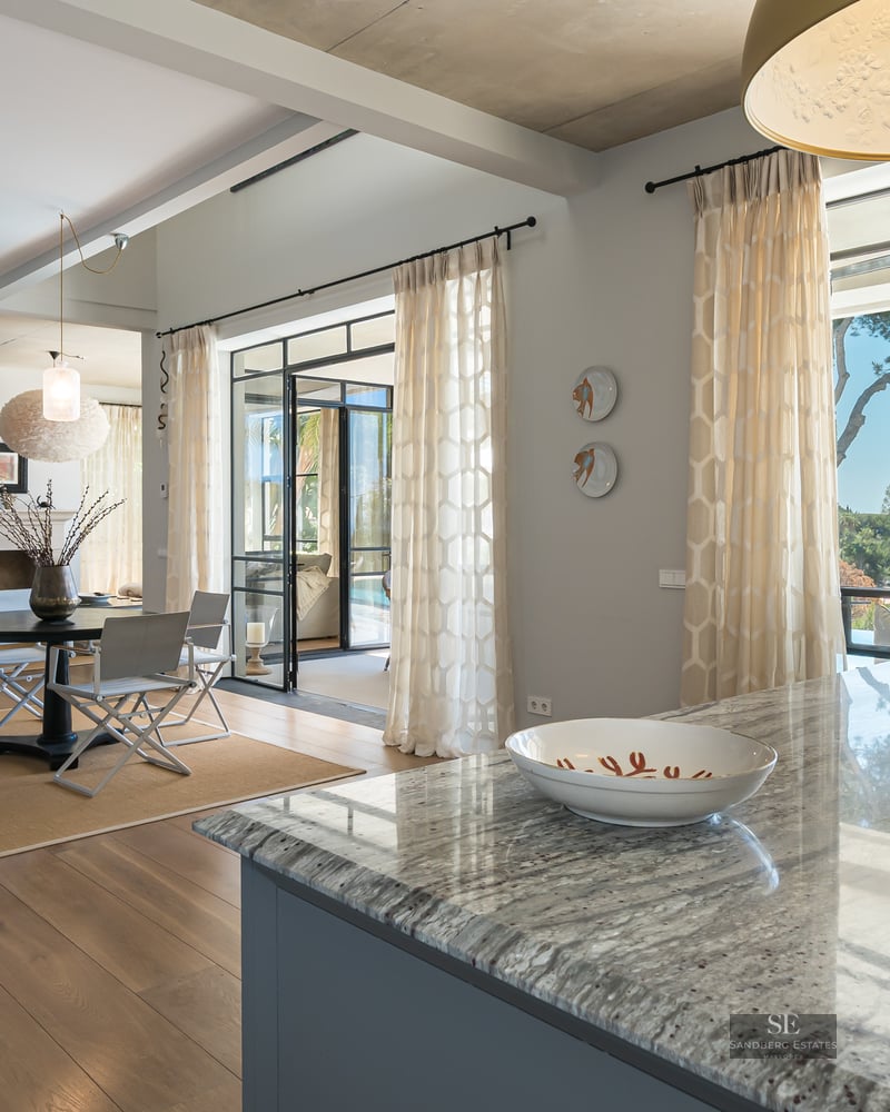 Designer living area featuring a marble island, black metal staircase, and large windows overlooking the sea.