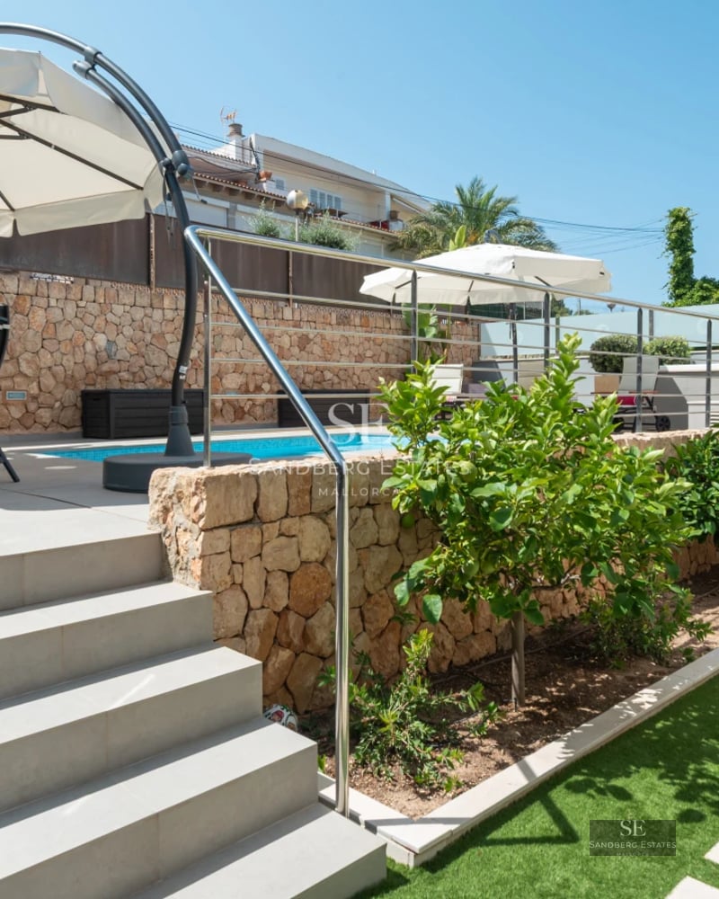 Spacious living room with floor-to-ceiling windows, light wood floors, modern fireplace, and garden views. Minimalist design with warm touches.