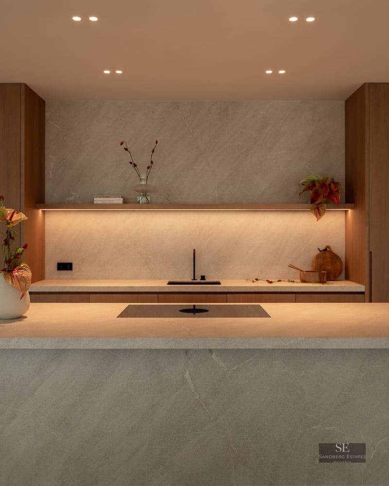 Modern kitchen featuring a large stone waterfall island, warm wood cabinetry, and integrated LED ambient lighting.