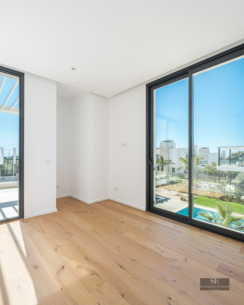 Empty room with light oak floors, white walls, and large glass sliding doors overlooking a terrace and swimming pool.