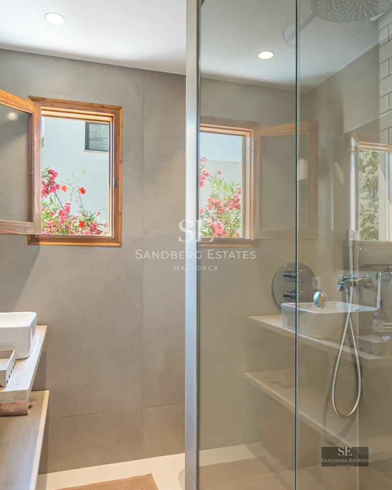 Spacious balcony with wood flooring, glass railing, and panoramic sea views. Modern and elegant furniture. Decorative plants.